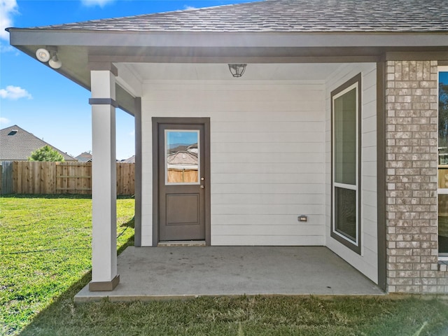 property entrance with a yard, fence, brick siding, and roof with shingles