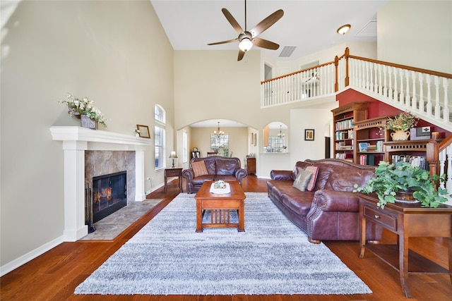 living area featuring visible vents, a tiled fireplace, ceiling fan with notable chandelier, wood finished floors, and arched walkways