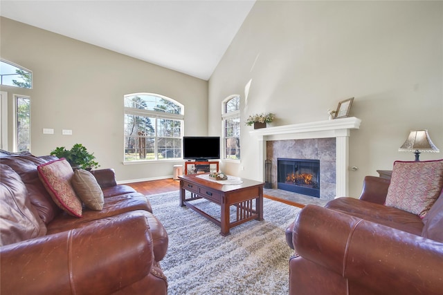 living room with baseboards, high vaulted ceiling, wood finished floors, and a tile fireplace