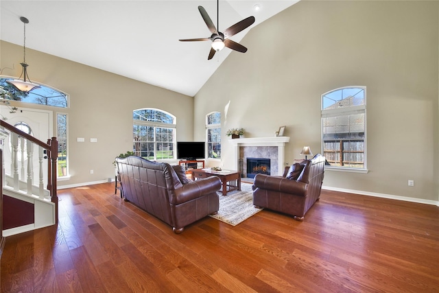 living area featuring stairway, wood finished floors, baseboards, high vaulted ceiling, and a fireplace