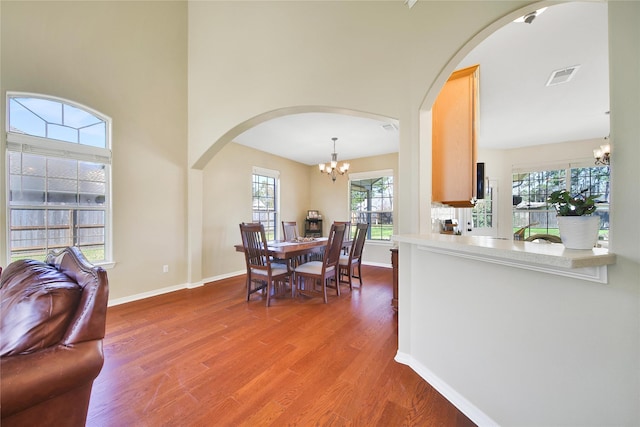 dining space with wood finished floors, baseboards, visible vents, arched walkways, and a notable chandelier