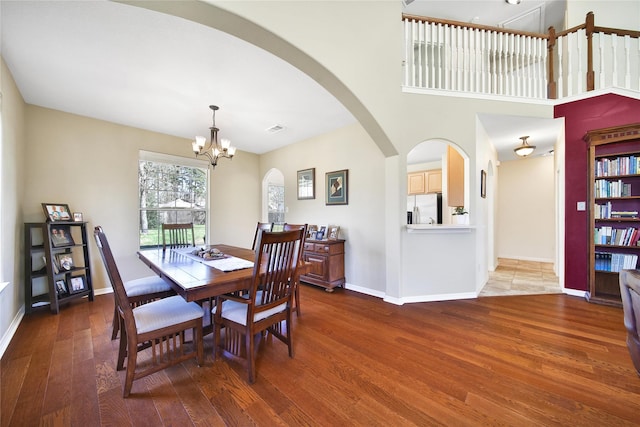 dining space featuring visible vents, baseboards, an inviting chandelier, wood finished floors, and arched walkways