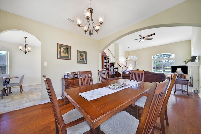 dining room with stairway, wood finished floors, visible vents, arched walkways, and ceiling fan with notable chandelier