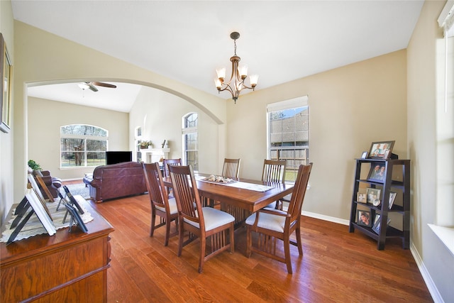 dining area with arched walkways, ceiling fan with notable chandelier, baseboards, and wood finished floors