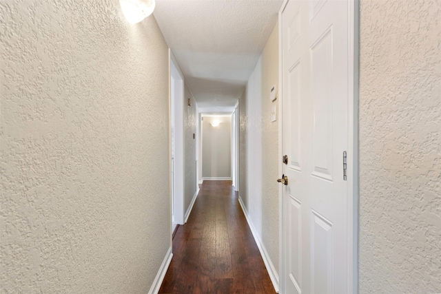 corridor with baseboards, a textured ceiling, dark wood finished floors, and a textured wall