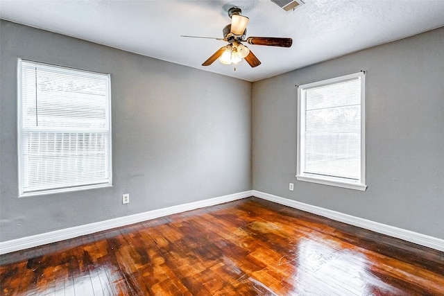 unfurnished room with a ceiling fan, dark wood-type flooring, visible vents, and baseboards