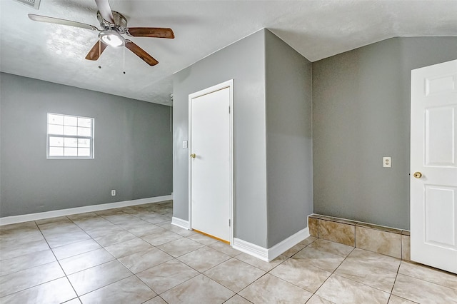 empty room featuring light tile patterned floors, baseboards, ceiling fan, and vaulted ceiling