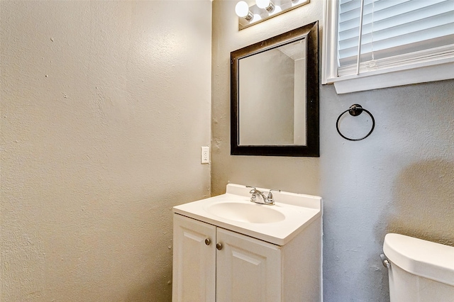 half bathroom with vanity, toilet, and a textured wall