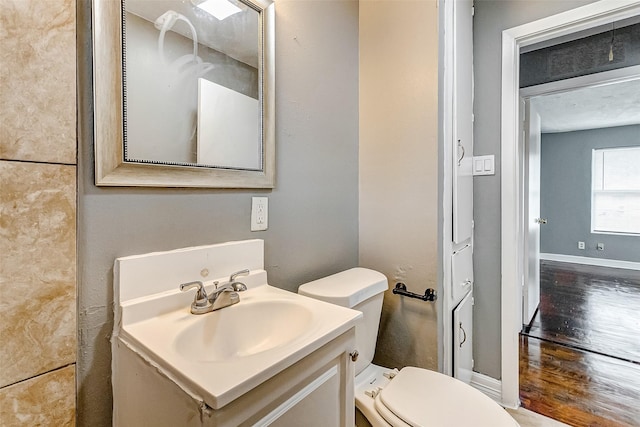 half bath featuring toilet, vanity, baseboards, and wood finished floors