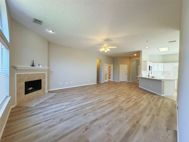 unfurnished living room with light wood-style flooring, a fireplace, visible vents, and ceiling fan