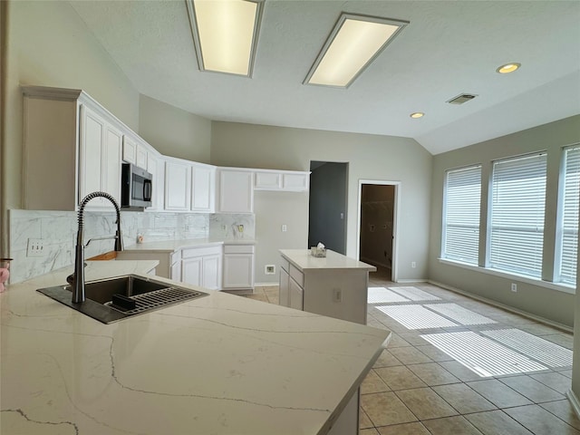 kitchen featuring visible vents, a sink, stainless steel microwave, backsplash, and light tile patterned floors