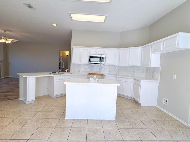 kitchen with light tile patterned floors, stainless steel microwave, a peninsula, and decorative backsplash