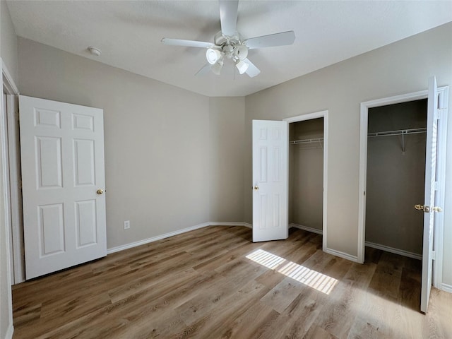 unfurnished bedroom with baseboards, two closets, wood finished floors, and a ceiling fan