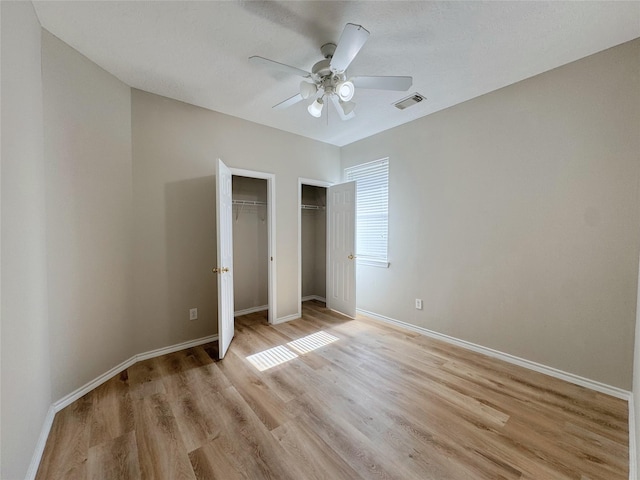 unfurnished bedroom with visible vents, light wood-style flooring, baseboards, and multiple closets