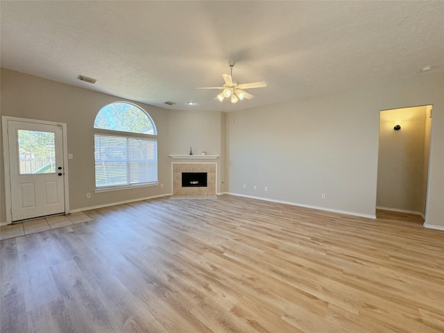 unfurnished living room with visible vents, baseboards, a fireplace, ceiling fan, and light wood-style floors