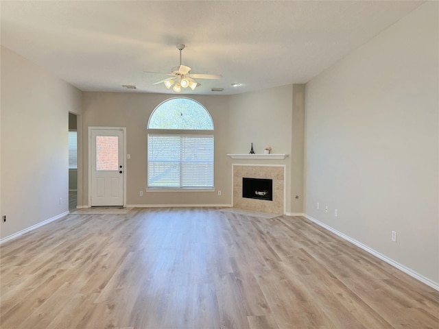 unfurnished living room with a tiled fireplace, baseboards, light wood-type flooring, and a ceiling fan