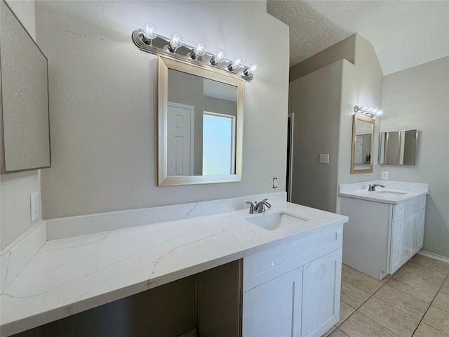 bathroom with a sink, a textured ceiling, two vanities, and tile patterned flooring