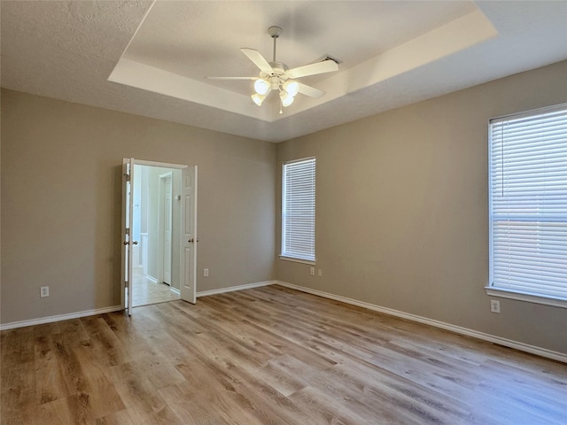 spare room with light wood-style flooring, baseboards, a tray ceiling, and a ceiling fan