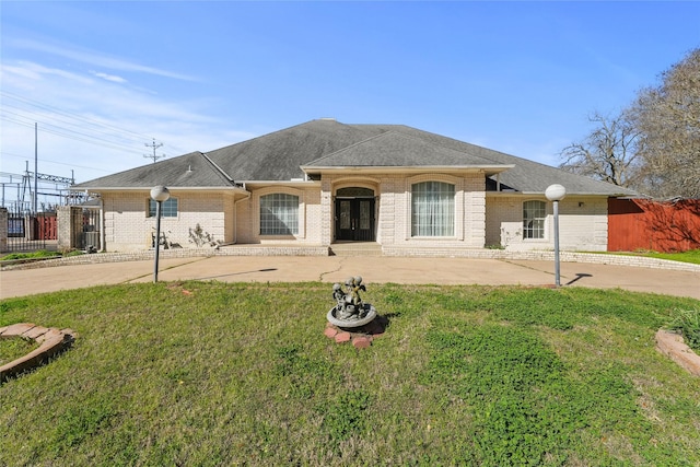 view of front of home with brick siding, roof with shingles, a front lawn, and fence