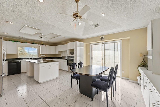 kitchen with dark countertops, visible vents, ceiling fan, a center island with sink, and black appliances