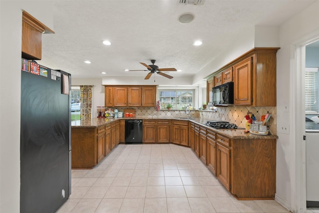 kitchen featuring brown cabinetry, dark stone countertops, black appliances, and backsplash