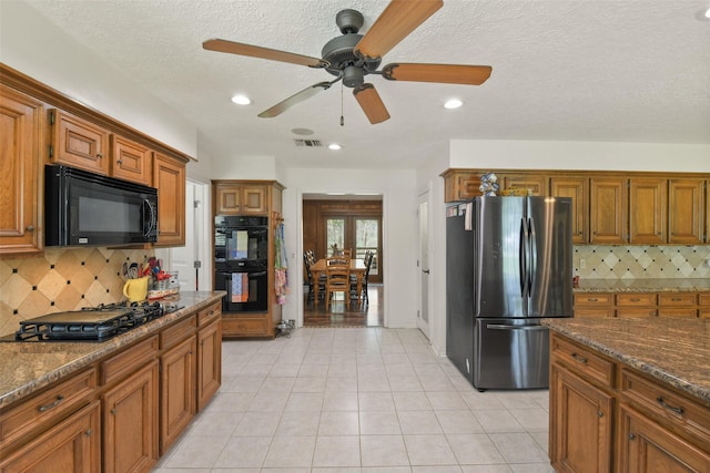 kitchen with visible vents, black appliances, dark stone countertops, brown cabinetry, and light tile patterned floors