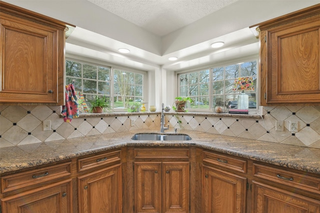 kitchen with a sink, dark stone countertops, and brown cabinetry