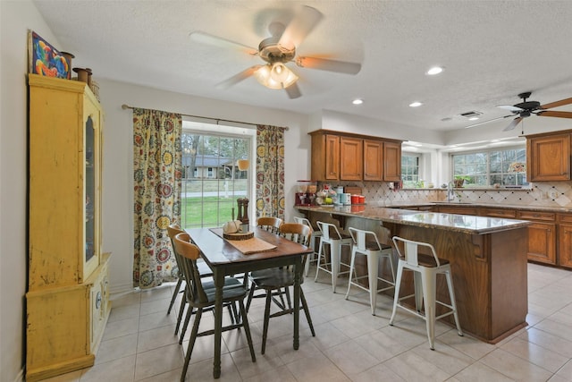 kitchen with brown cabinets, a peninsula, dark stone counters, a kitchen breakfast bar, and tasteful backsplash