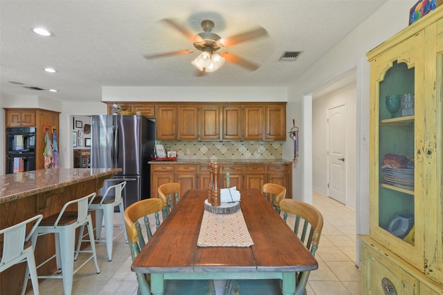 kitchen featuring light tile patterned floors, visible vents, freestanding refrigerator, dobule oven black, and backsplash