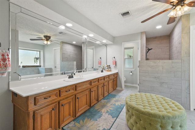 bathroom featuring double vanity, visible vents, a tile shower, and a sink