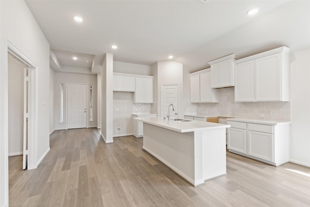 kitchen featuring a sink, a center island with sink, decorative backsplash, white cabinetry, and light wood-style flooring