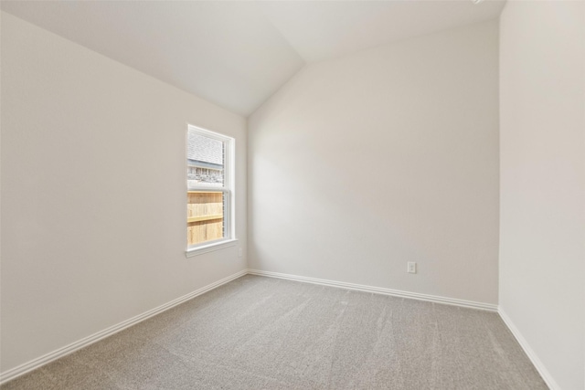 carpeted empty room featuring vaulted ceiling and baseboards