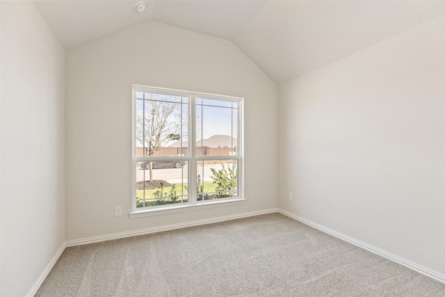 carpeted empty room featuring vaulted ceiling and baseboards