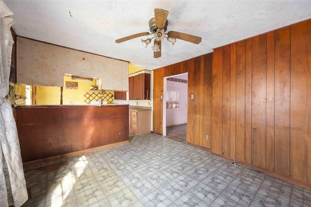 kitchen with tile patterned floors, wood walls, a textured ceiling, and a ceiling fan