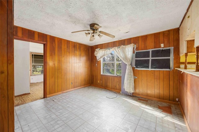 empty room with wood walls, a textured ceiling, and a ceiling fan