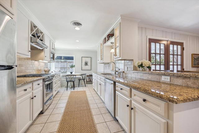 kitchen featuring glass insert cabinets, ornamental molding, a sink, decorative backsplash, and appliances with stainless steel finishes