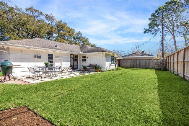 rear view of property with a fenced backyard, a yard, a shingled roof, brick siding, and a patio area