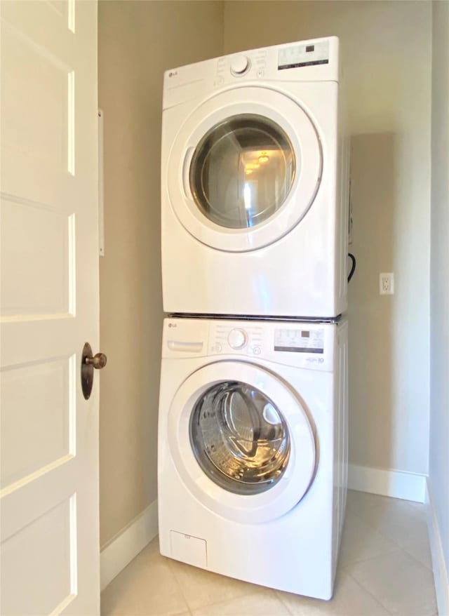 washroom featuring laundry area, light tile patterned floors, baseboards, and stacked washer and clothes dryer