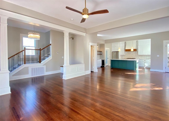 unfurnished living room featuring baseboards, visible vents, ornate columns, dark wood-style flooring, and stairs