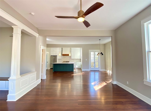 unfurnished living room with dark wood-style floors, baseboards, a ceiling fan, and ornate columns