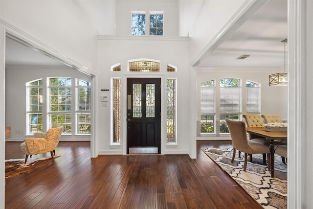 foyer with wood finished floors, visible vents, a towering ceiling, and ornamental molding