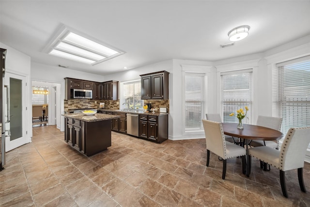 kitchen with tasteful backsplash, dark brown cabinets, appliances with stainless steel finishes, and a center island