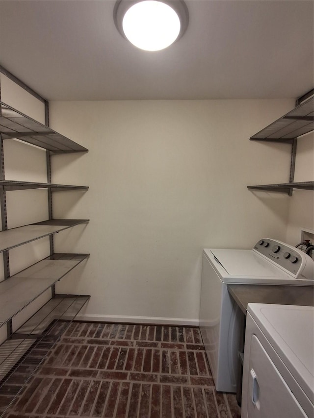 washroom featuring brick floor, baseboards, separate washer and dryer, and laundry area