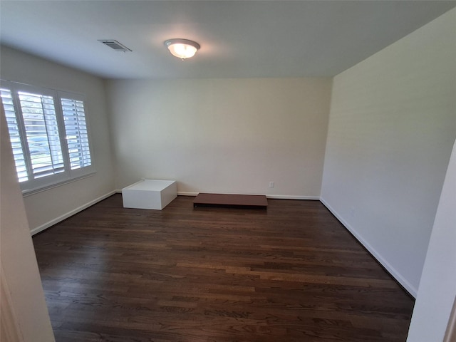 unfurnished room featuring visible vents, baseboards, and dark wood-style floors