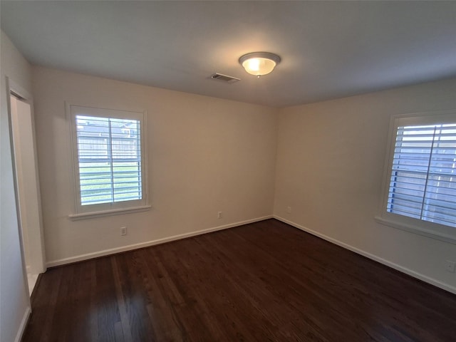 unfurnished room with visible vents, dark wood-type flooring, and baseboards