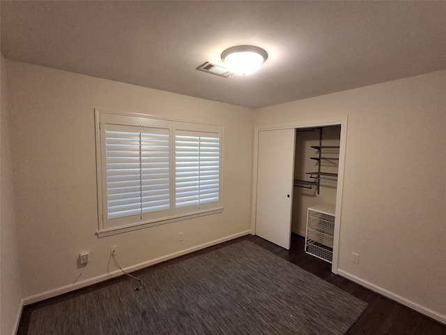 unfurnished bedroom with visible vents, baseboards, a closet, and dark wood-style flooring