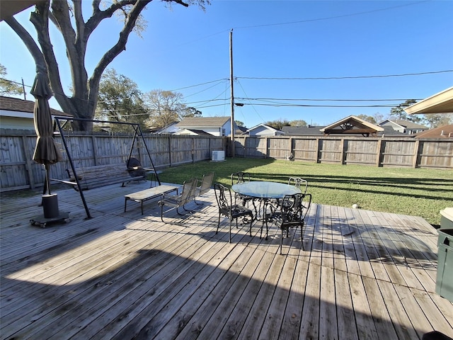 wooden terrace with outdoor dining area, a lawn, and a fenced backyard