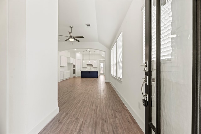 interior space with visible vents, wood finished floors, baseboards, arched walkways, and lofted ceiling