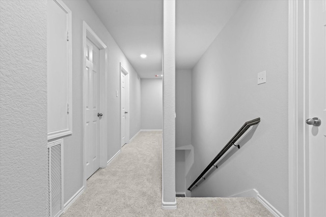 corridor featuring an upstairs landing, visible vents, baseboards, and carpet floors