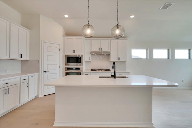 kitchen with a sink, under cabinet range hood, tasteful backsplash, appliances with stainless steel finishes, and white cabinets